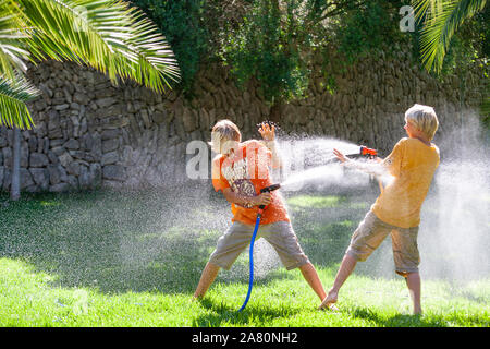 Frères jouant avec tuyaux de jardin Banque D'Images