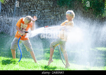 Frères jouant avec tuyaux de jardin Banque D'Images