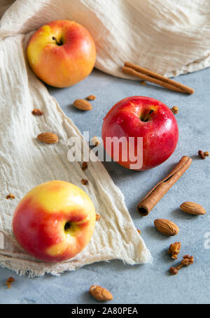 Trois pommes de couleur rouge et jaune avec des bâtons de cannelle, les amandes se situent sur une base de béton gris beige avec un chiffon doux. Orientation verticale. Banque D'Images