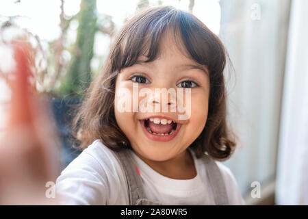 Smiling little girl prenant un tout en jouant à la maison selfies Banque D'Images