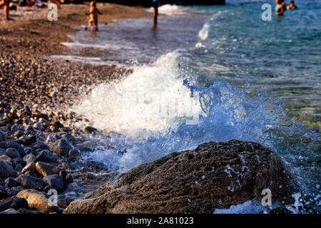 Frozen splash de la mer vague sur un rocher sur la plage de la mer sur l'arrière-plan de personnes au repos dans le flou. Banque D'Images