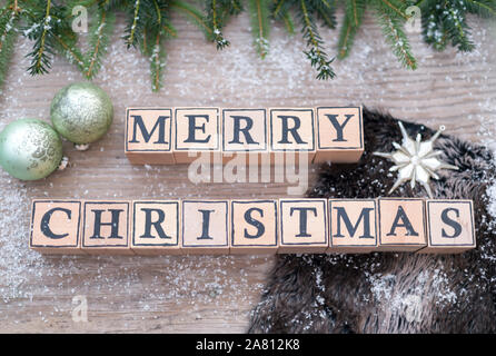 Cubes en bois avec des lettres forme le texte anglais Joyeux Noël. Ils sont couchés sur un fond de bois. Branches de sapin et boules de Noël sont à côté. Banque D'Images