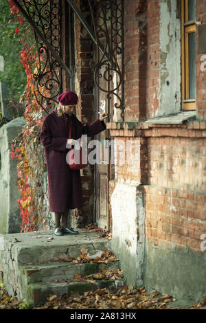 Femme avec une lettre frappe à la porte d'une maison ancienne. Banque D'Images