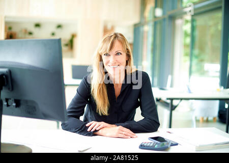 Portrait of smiling mature woman vente assis derrière son ordinateur au bureau 24. Banque D'Images