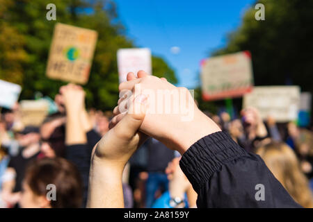 Deux jeunes gens lors d'un rassemblement, joindre les mains ensemble la paix, l'unité de signalisation et de l'esprit devant une foule portant des pancartes de protestation Banque D'Images