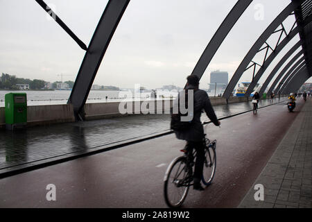 Motion floue image de l'homme monter sur un vélo à l'arrière de la gare principale appelée Amsterdam Centraal. C'est un jour d'été pluvieux. Banque D'Images