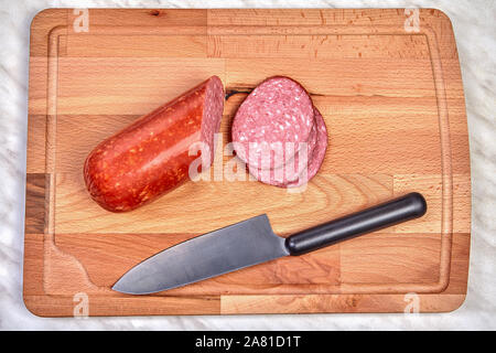 Des morceaux de saucisse hachée et un couteau de cuisine, s'allonger sur une planche à découper en bois. Banque D'Images