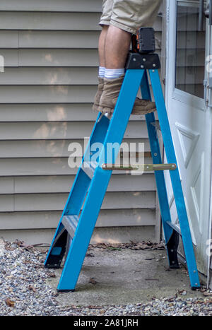 Un travailleur se dresse sur un escabeau comme il travaille à l'extérieur sur l'extérieur d'une maison Banque D'Images