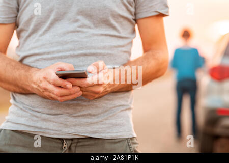 Man texting assistance routière pour véhicule est tombé en panne après le coucher du soleil en automne, selective focus Banque D'Images