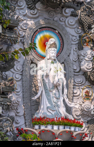 Da nang, Vietnam - 10 mars 2019 : Chua Long un temple bouddhiste chinois. Gros plan du Guan Yin statue en pierre grise. Les fleurs rouges à ses pieds, des fo Banque D'Images
