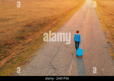 Woman pulling suitcase voyage assurance sur la route en automne coucher du soleil, high angle view de drone pov Banque D'Images