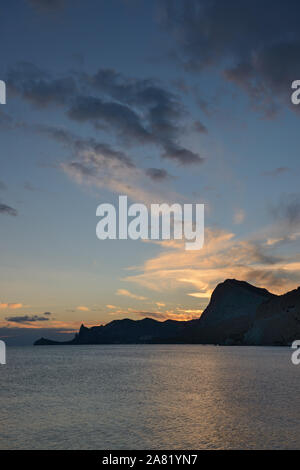 Vue sur la côte de Sudak ville plage vers la montagne Sokol et Novy Svet (Nouveau Monde) emplacement dans des nuages coucher de soleil en contre-jour, la Crimée, la Russie. Banque D'Images