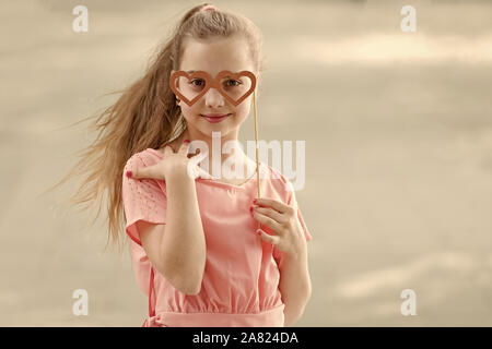 Valentines adorable fille. Cute kid holding fancy Valentines Day party props sur stick. Petit enfant regardant à travers des lunettes en forme de coeur le Jour de Valentines. Happy valentines day, copiez l'espace. Banque D'Images