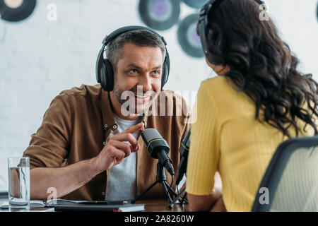 Smiling radio host des gestes tout en parlant de collègue en studio de diffusion Banque D'Images