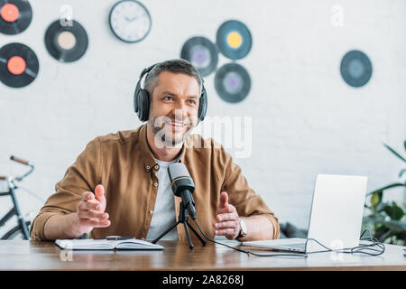 Cheerful radio host des gestes tout en parlant dans le microphone dans un studio de diffusion Banque D'Images