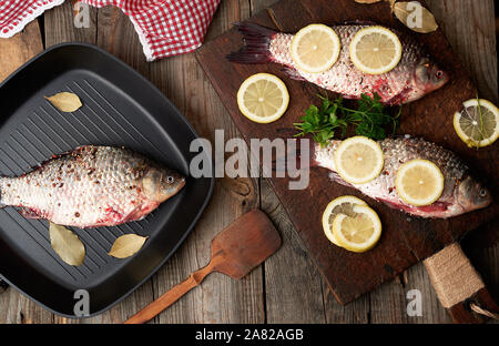 Poisson frais dans le carassin pèse-personne sur une vieille planche à découper en bois brun, de l'alimentation assaisonné d'épices et des tranches de citron, vue du dessus Banque D'Images