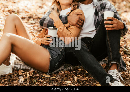 View of a young couple holding thermo tasses alors qu'il était assis sur le feuillage d'automne Banque D'Images