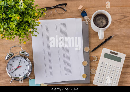 Vue de dessus de table en bois avec document, tasse à café, réveil, clés de maison, calculatrice et plante verte Banque D'Images