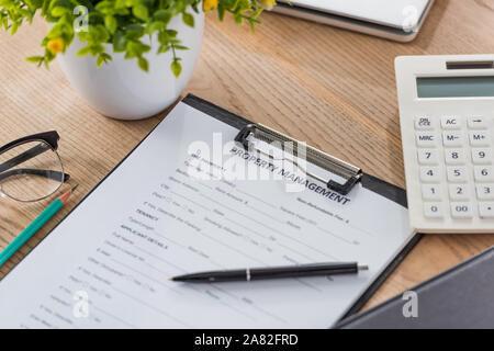 Presse-papiers avec l'accord de gestion immobilière, stylo, calculatrice et plante verte sur le bureau en bois Banque D'Images