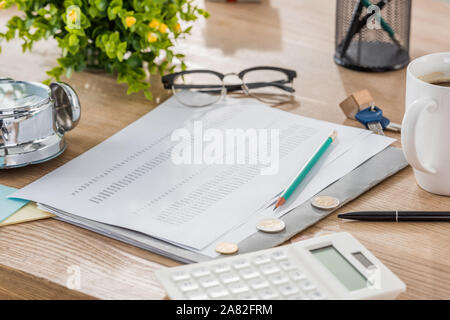 Près de calculatrice, papier monnaie, tasse de café, verres, plante verte et chambre modèle sur table en bois Banque D'Images