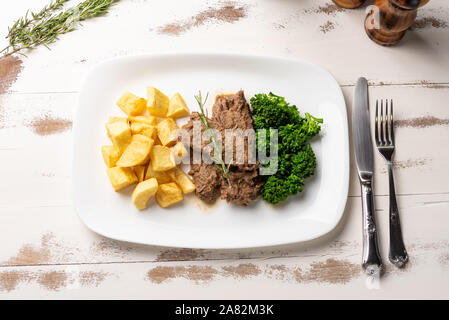 Ragoût de boeuf avec des pommes de terre rustique et le brocoli dans une assiette blanche sur fond de table en bois blanc, lumière douce Banque D'Images
