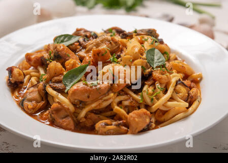 Pâtes aux fruits de mer en plaque blanche sur un fond de bois blanc, lumière douce. Spaghettis ai Frutti di mare, fruits de mer gastronomie méditerranéenne Banque D'Images