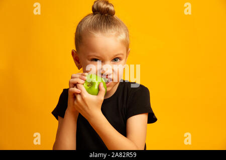 Happy girl eating apple vert, gros plan jolie fille bits apple frais isolé sur fond jaune Banque D'Images