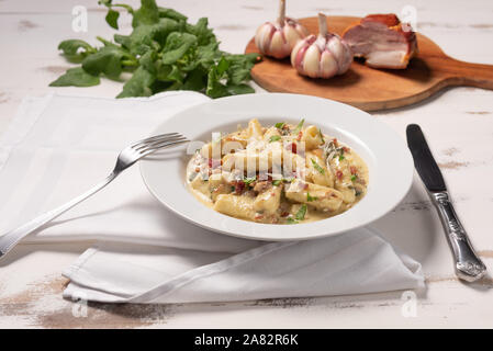 Pâtes penne avec sauce carbonara en plaque blanche sur fond blanc en bois, lumière douce, l'angle de vue. La cuisine Italienne Banque D'Images