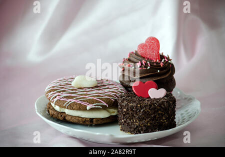 Trois pâtisseries décadentes sont sur une plaque pour le plus doux l'un que vous aimez. Un chocolat whoopee pie, gâteau cupcake framboise et dépoli Banque D'Images