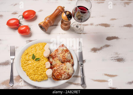 Risotto au safran avec parmigiana boeuf steak. Risoto et le boeuf dans une assiette blanche sur fond blanc en bois. Lumière douce. Cuisine italienne. Risotto avec curcum Banque D'Images