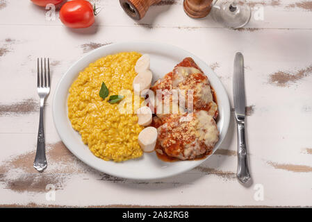 Risotto au safran avec parmigiana boeuf steak. Risoto et le boeuf dans une assiette blanche sur fond blanc en bois. Lumière douce. Cuisine italienne. Risotto avec curcum Banque D'Images