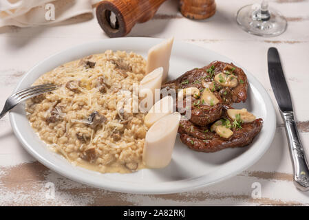 Risotto avec du filet mignon. Risoto et le bœuf avec les câpres et les champignons dans une assiette blanche sur fond blanc en bois. Cuisine italienne. Banque D'Images