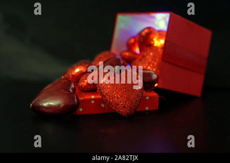 Happy Valentines Day déversant des formes à partir de l'éclairage coloré intérieur d'une boîte cadeau rouge sur un fond noir avec selective focus Banque D'Images