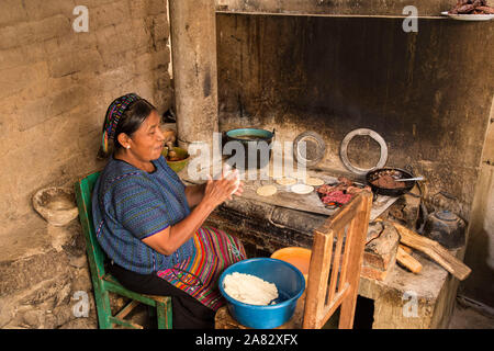 Une femme portant robe Maya typique fait plus de tortillas un poêle à bois dans la cuisine de sa maison à San Antonio Palopo, au Guatemala. Banque D'Images