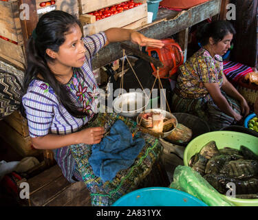 Jolie jeune femme en costume traditionnel Maya la vente de poisson Tilapia dans le marché à Santiago Atitlan, Guatemala. Elle utilise une balance à main sca Banque D'Images