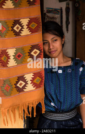 Une jolie jeune fille Maya portant robe typique regarde par la porte de l'atelier de tissage de la famille à San Antonio Palopo, au Guatemala. Banque D'Images