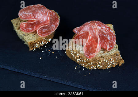 Vue de dessus les tranches de salami sur une tranche de pain complet sur fond sombre Banque D'Images