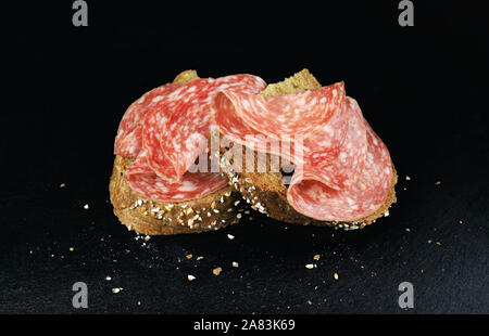 Vue de dessus les tranches de salami sur une tranche de pain complet sur fond sombre Banque D'Images