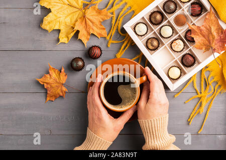 Woman's hands holding une tasse de café noir foulard orange boîte de chocolats sur un fond d'automne. Vue supérieure de la télévision mise en page. Copier l'espace. F horizontal Banque D'Images