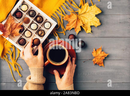 Woman's hands holding une tasse de café noir foulard orange boîte de chocolats sur un fond d'automne. Vue supérieure de la télévision mise en page. Copier l'espace. F horizontal Banque D'Images