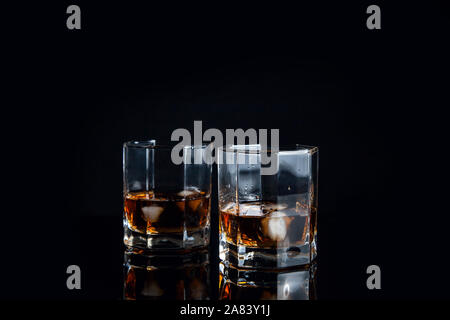 Les boissons alcoolisées et la conception. Deux verres de whisky avec des glaçons on reflective surface noire. Banque D'Images