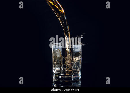 Verser dans un verre à whisky avec de la glace réfléchissante isolé sur la surface noire. Splash de whisky en verre, de nombreuses gouttes de boissons de verre. Banque D'Images