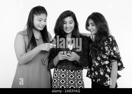 Studio shot of three young friends smiling woman Persan tout en utilisant un téléphone mobile ensemble Banque D'Images