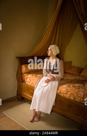 Style Vermeer portrait d'une jeune femme en costume renaissance assis sur un lit d'époque avec son travail de broderie Banque D'Images