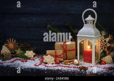 Décoration de Noël avec une bougie Lanterne lumière, cadeaux, sapins de Noël, branches et gingerbread stars organisés contre un arrière-plan en bleu foncé, c Banque D'Images