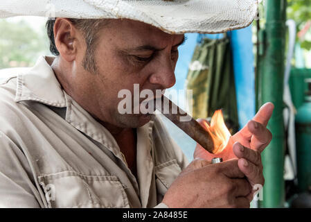 Un agriculteur/propriétaire cubain portant un chapeau cubain traditionnel allume son cigare roulé à la main à l’aide d’un briquet, dans la Valle de Vinales, province de Pinar del Río, a Banque D'Images