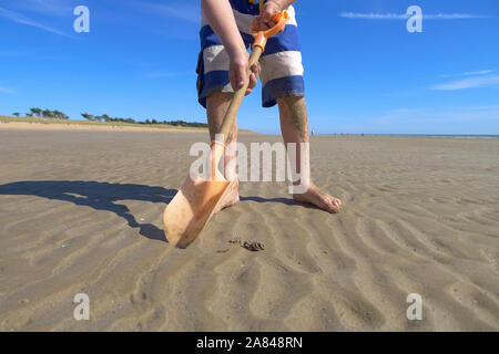 Un jeune garçon creusant dans le sable sur la plage, en France. Banque D'Images