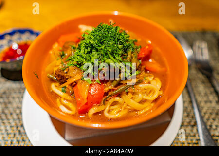 Kazakhstan traditionnelles savoureuses Lagman avec viande d'agneau et de légumes servi dans un bol de couleur orange Banque D'Images