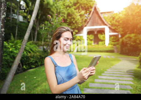 Sunshine portrait of young woman using tablet and smiling on green palms et maison historique en Thaïlande Banque D'Images