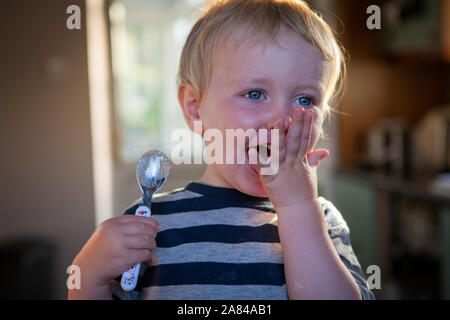 Un jeune garçon riant comme il tient une cuillère faisant de la cuisson à la maison. Banque D'Images